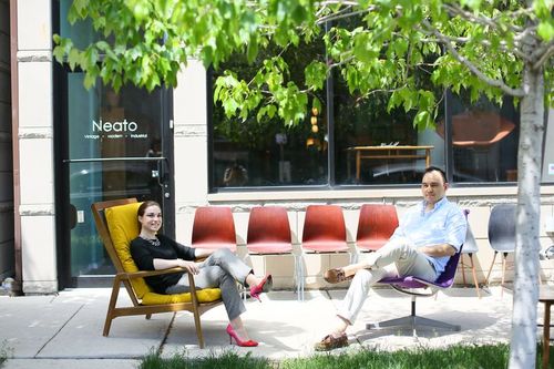 Jesse and Caitlin pose in colorful accent chairs in front of their furniture store Neato