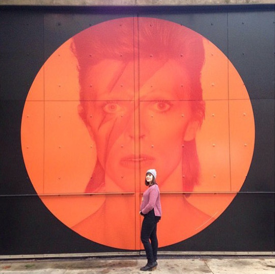 Jaime Rovenstine poses in front of an orange and red Bowie mural