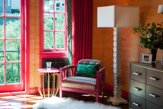 Pink accent chair in orange room with pink drapes, white fluffy rug