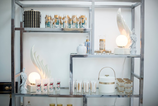 Chrome and glass bookshelf with gold-accented glassware and 70s table lamps