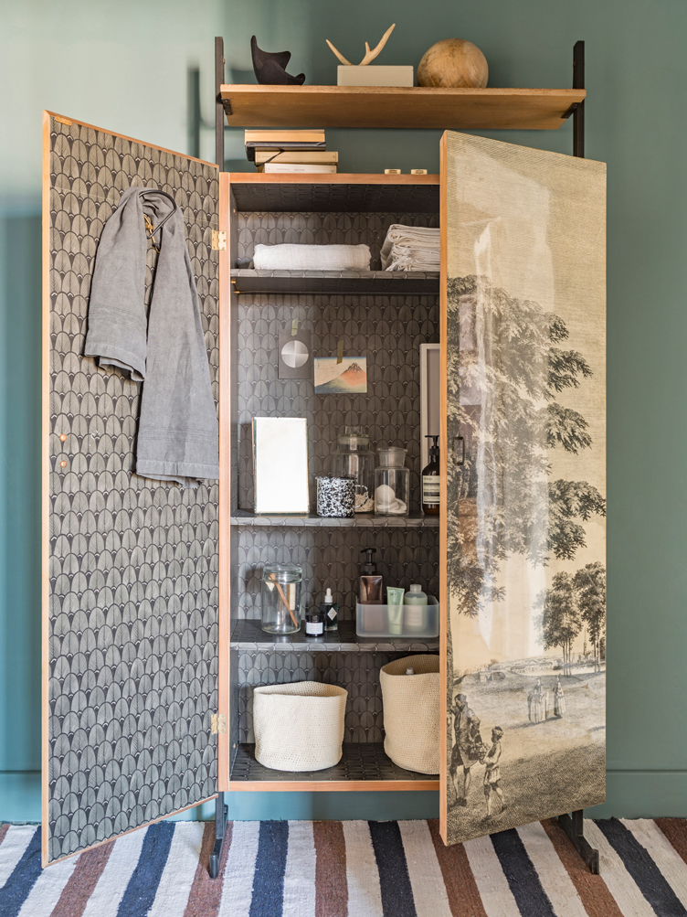 A painted wardrobe is opened up to reveal graphic wallpaper and shelves of toiletries 