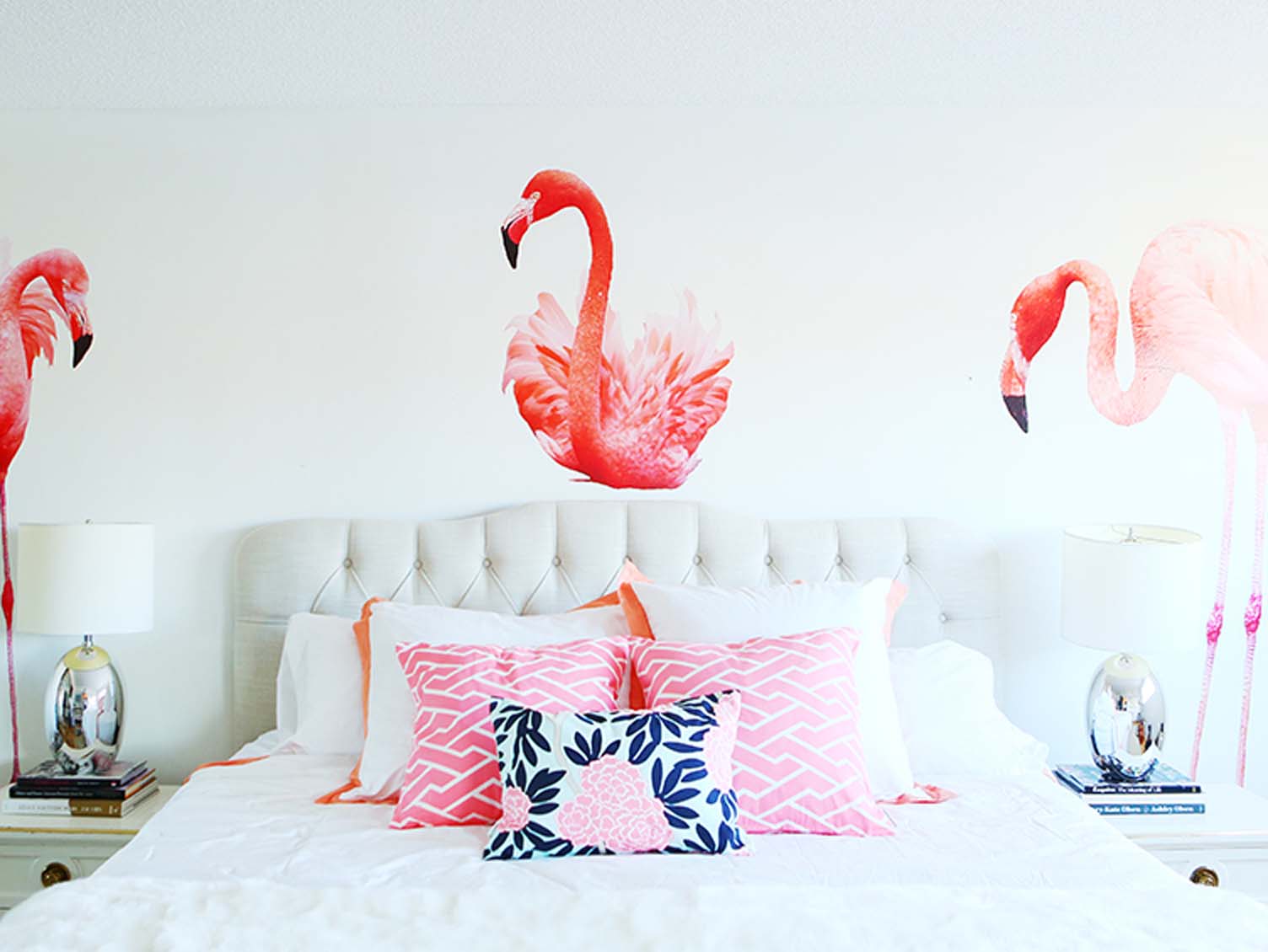 Bedroom with white upholstered headboard, pink pillows, and flamingo wallpaper.