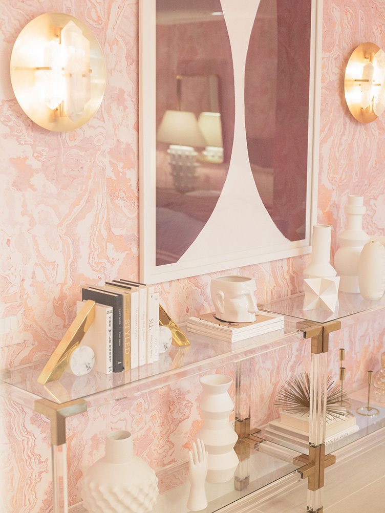 Assorted decor on clear, modern shelves, and abstract art in pink bedroom