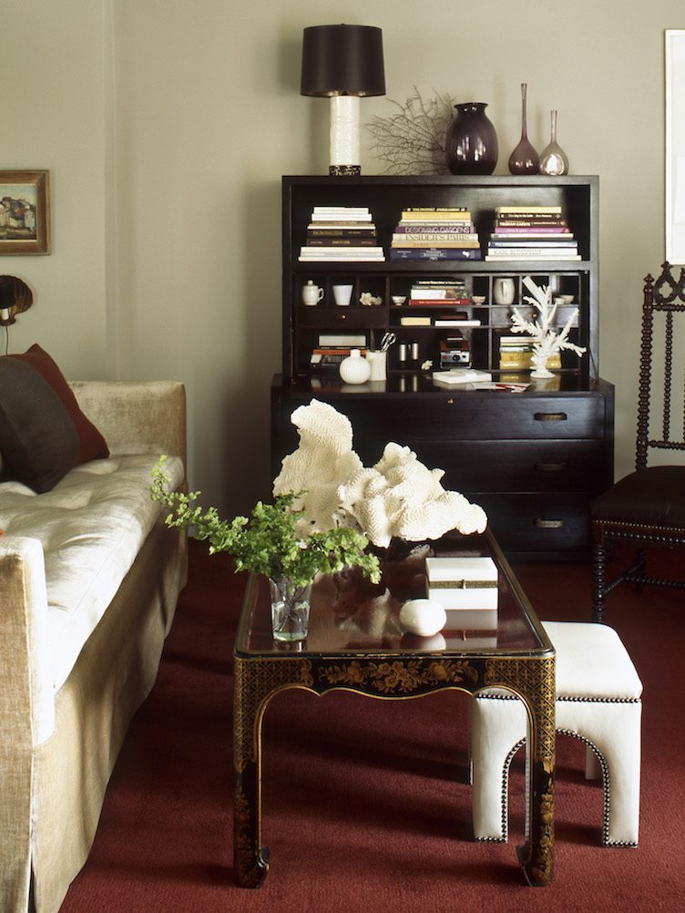 A secretary desk in a traditional living room with neutral colors and a coffee table with classic decor.