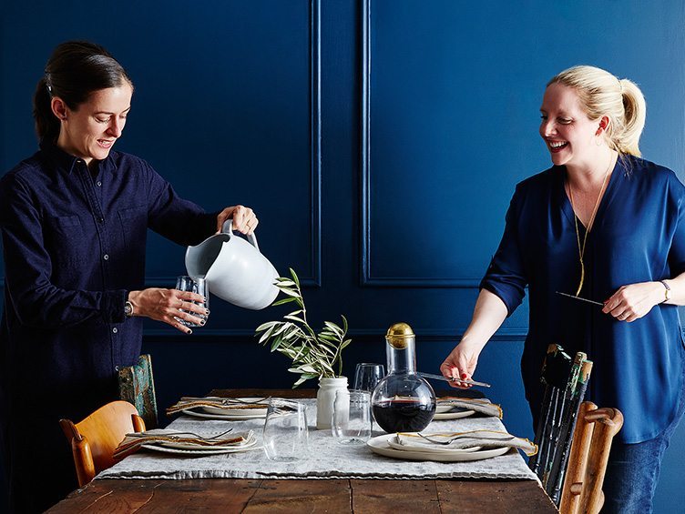 Merrill Stubbs and Amanda Hesser set a table in front of royal blue paneled walls.