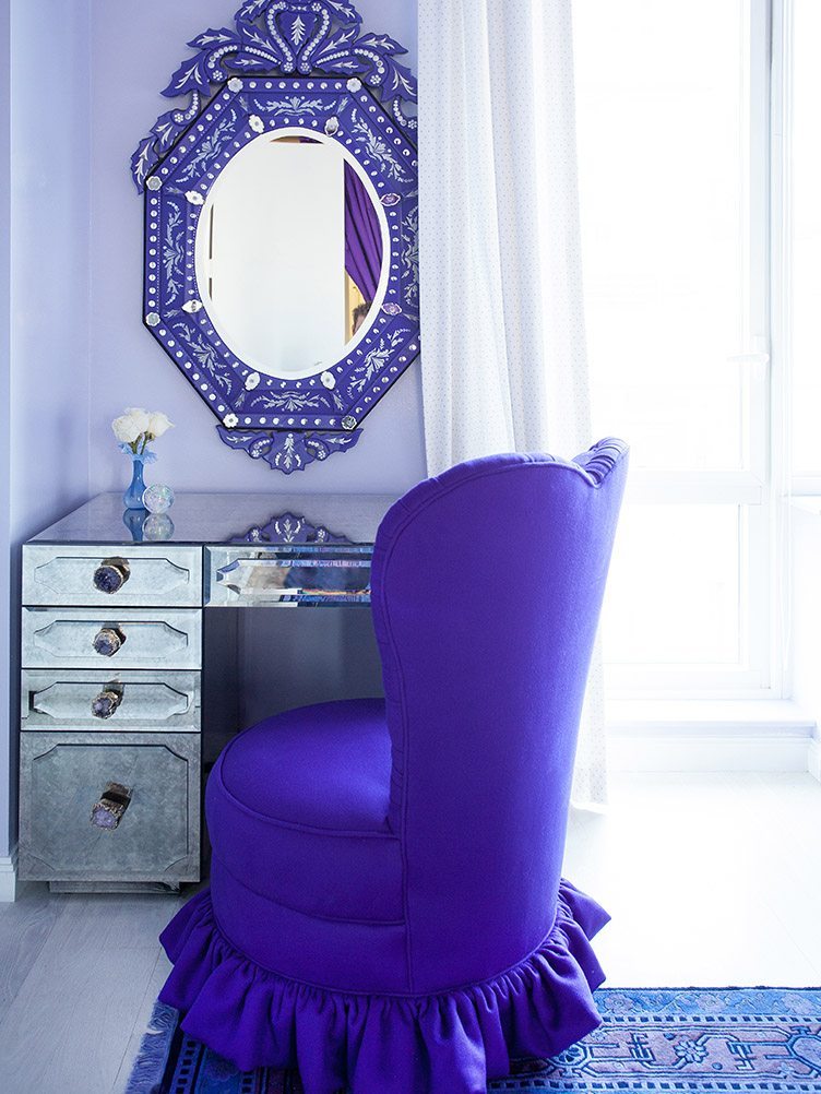 Glamorous workspace with a mirror desk, large purple mirror and a purple slipper chair.