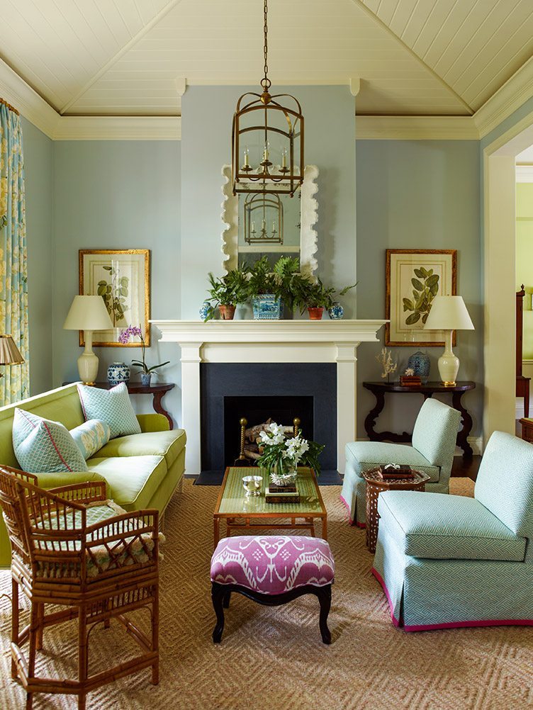 Beach house living room with a hanging chandelier, rattan chair, and blue slipper chairs to match the blue walls.