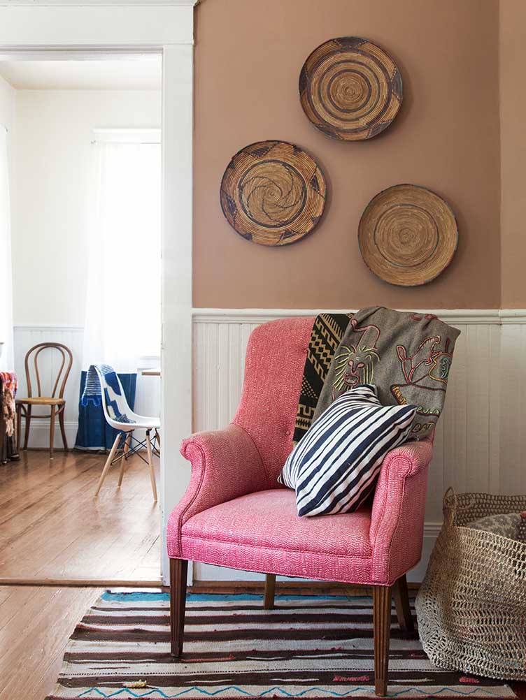 Pink accent chair, and hanging woven mats over striped rug