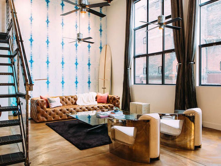 Leather tufted couch compliments the futuristic gold accent chairs and indigo dyed-style wallpaper.