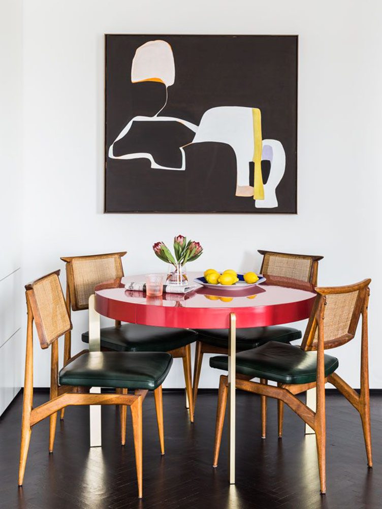 Dining room with red round dining table and rattan dining chairs with black leather seats