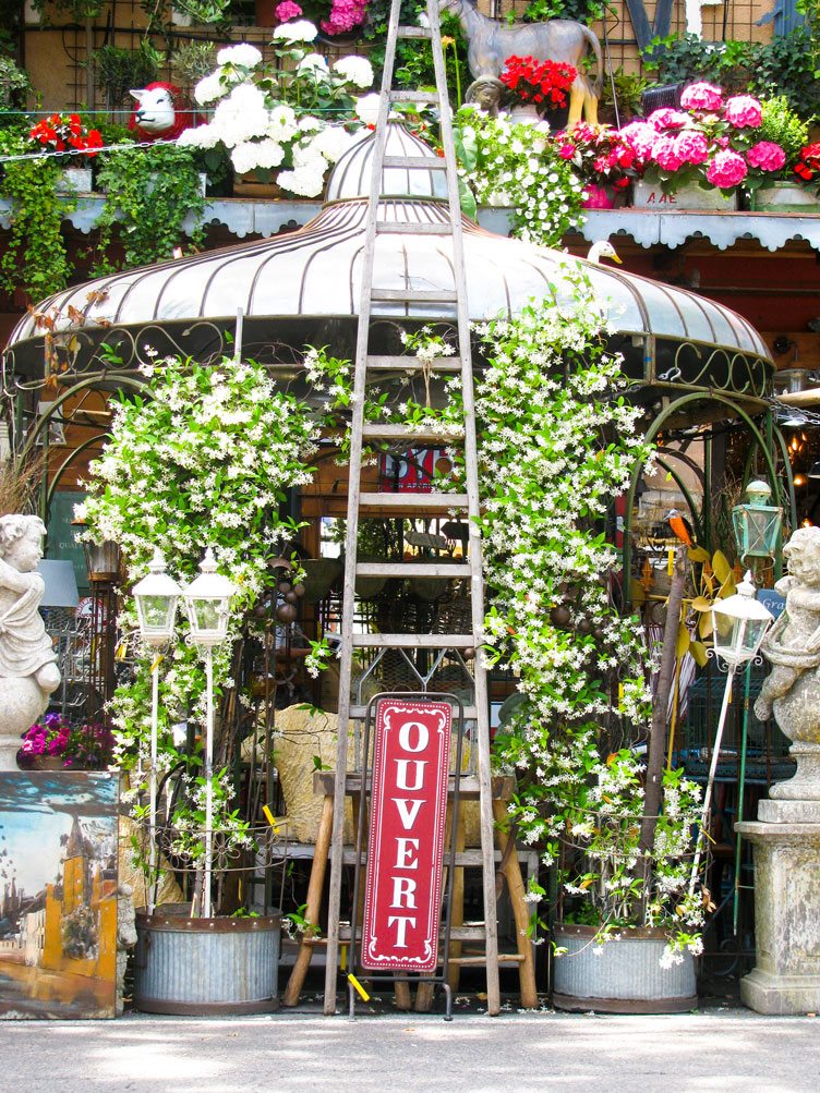 Antique sale with assorted metal goods and oversized plants.