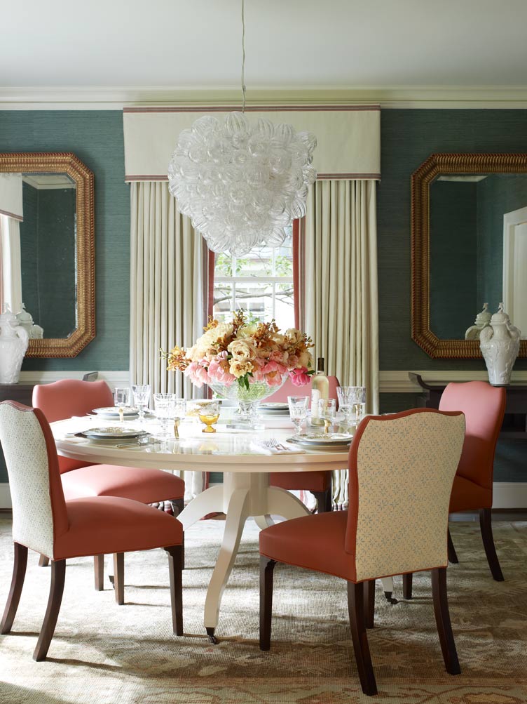 Traditional dining room with glass chandelier, pink dining chairs, and blue wallpaper 