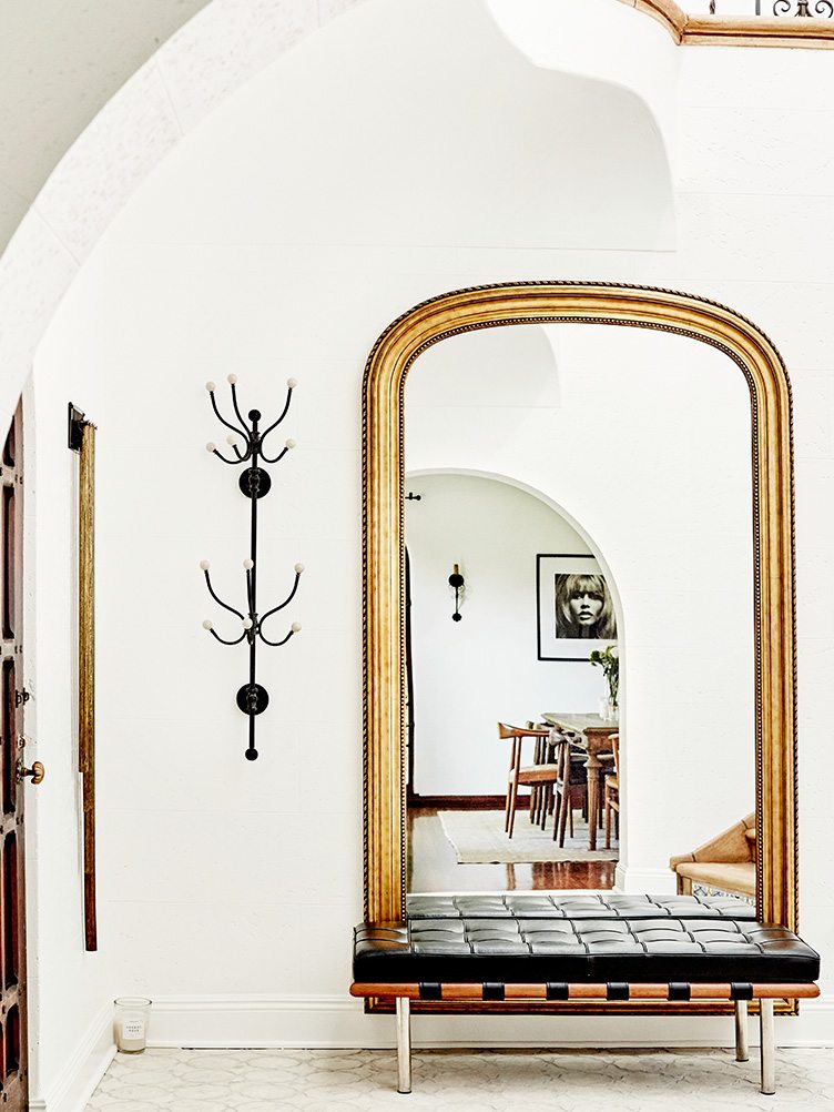 Bright entryway with black leather bench and gold-framed mirror