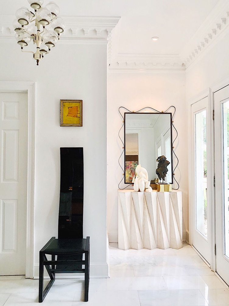 Modern entryway with black accent chair and white sculpted side board 