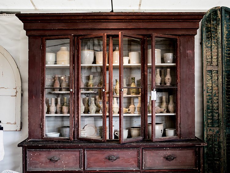 Wooden cabinet with glass doors and shelves of ceramic jars, pots, and vases