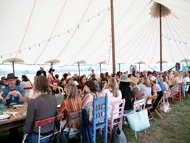 Guests sit for dinner under large white tent in mismatched chairs at Rancho Pillow dinner party