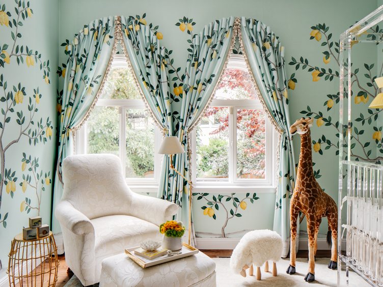 Baby nursery with lemon-tree wallpaper and matching drapes with white accent chair.