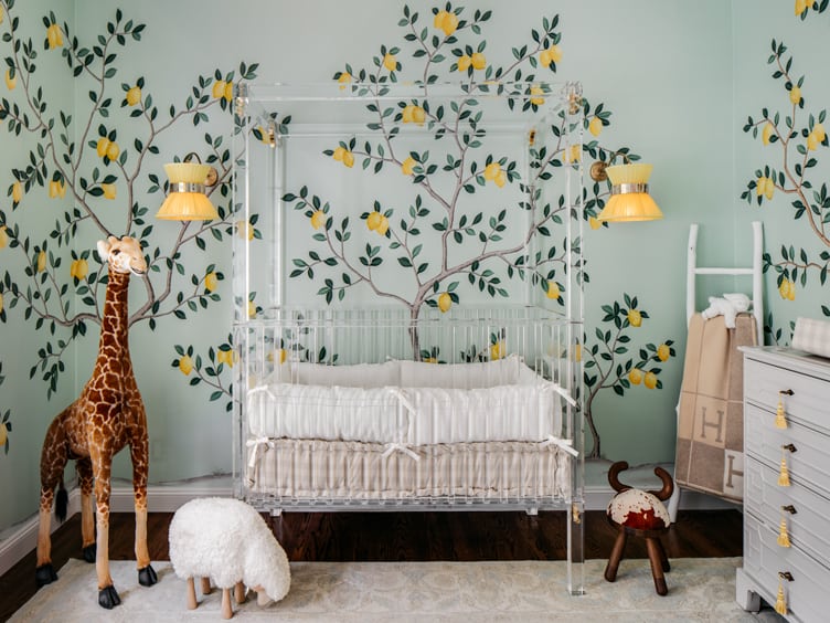 Transparent crib, and baby blue dresser in nursery with lemon-tree wallpaper