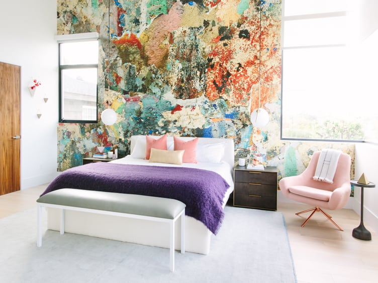 Bedroom with abstract-painted accent wall and pink mid-century accent chair.