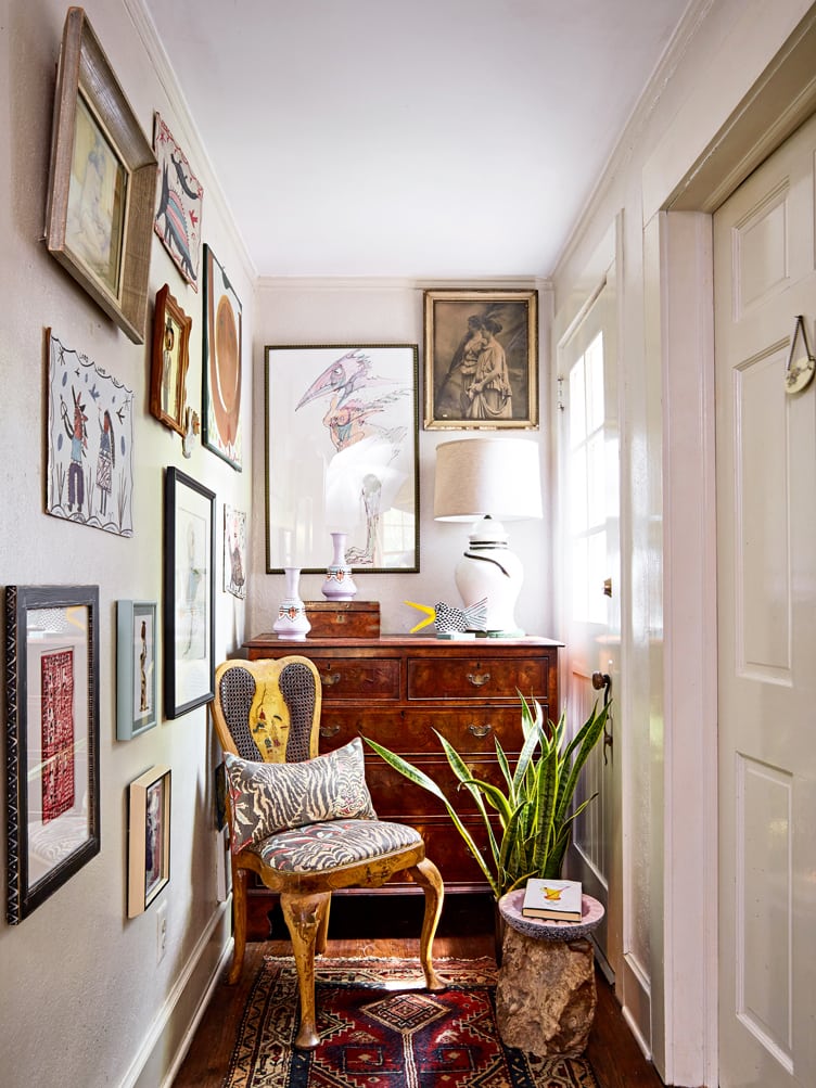 Collection of abstract, impressionist, and portraits with accent chair and wooden dresser in hallway