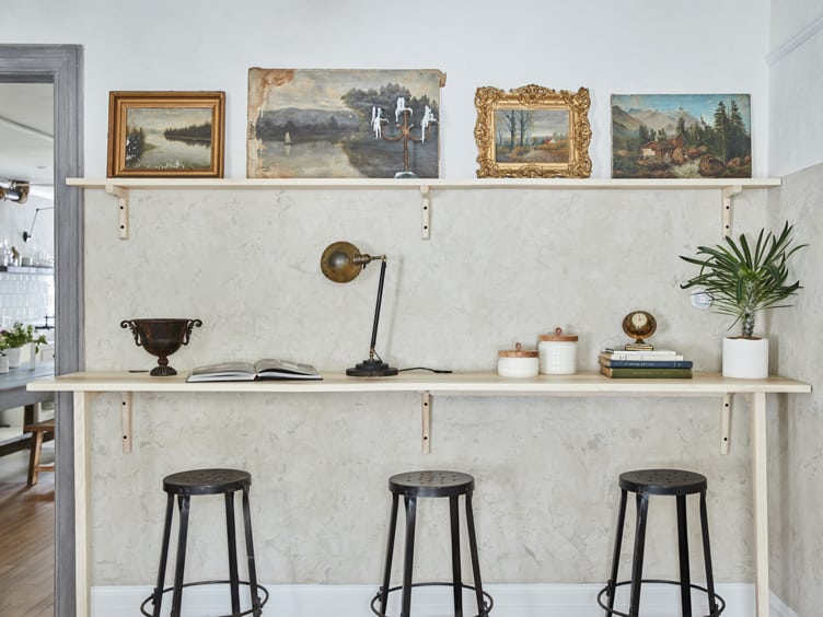 Organic Modern Home Bar with Black Metal Stools and Minimalist Shelves Holding Vintage Artwork.