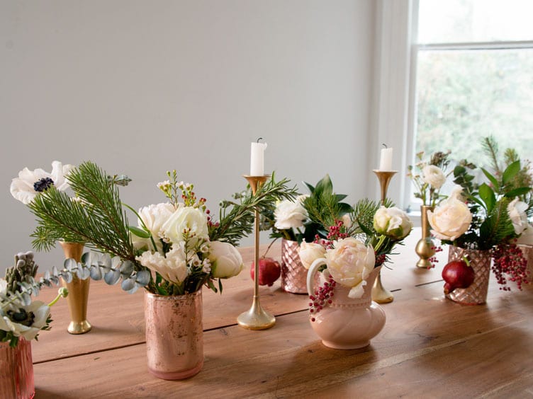 Wood table topped with assorted floral arrangements and copper candlesticks