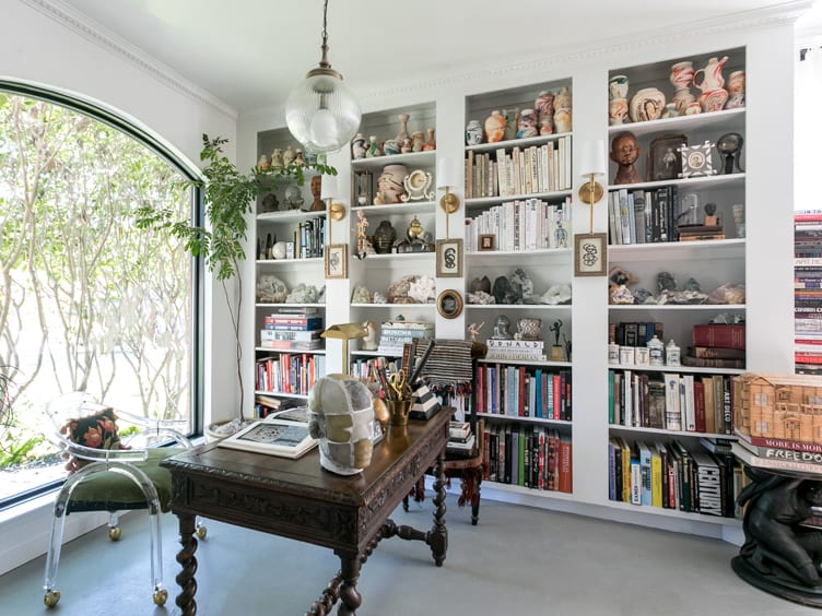 Eclectic Home Office with Human Face Sculptures, Vintage Clay Pots, Ornate Desk, and Acrylic-Armed Chair.