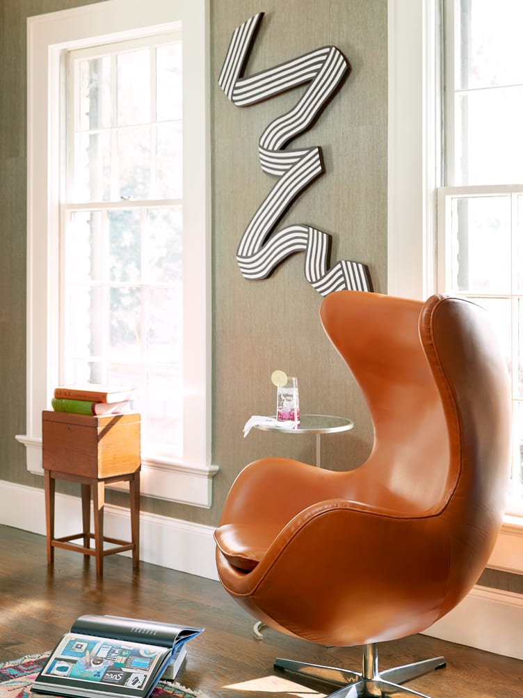 A classic leather egg chair with a ribbon-like wall hanging on textured wallpaper.