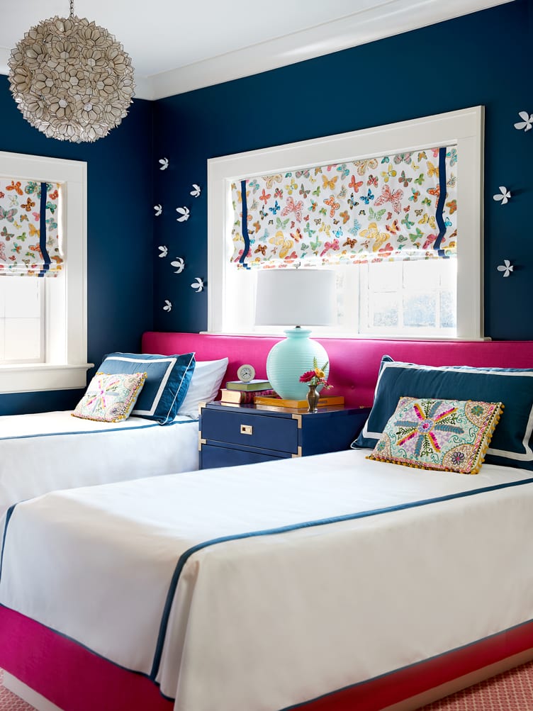 Girls bedroom with dark blue walls and matching white and blue beds with pink headboard.