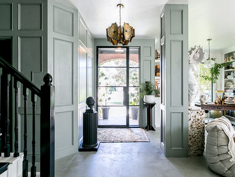 Green paneled entryway, Brutalist chandelier, pedestal with bust, cement floors, eclectic decor
