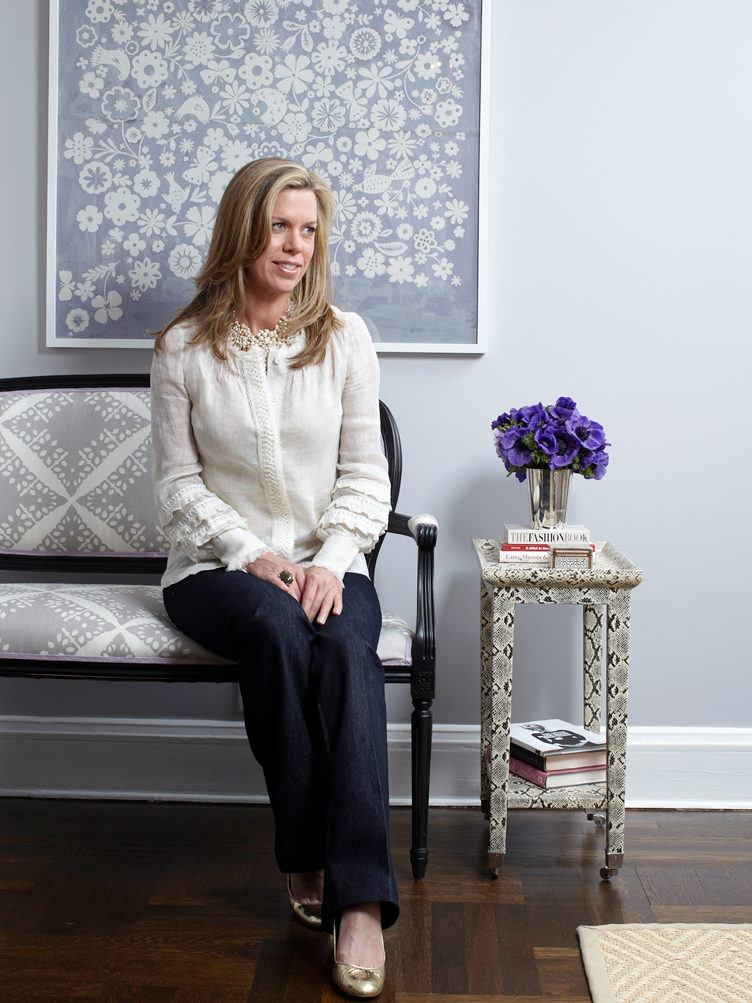 Ashely Whittaker poses on upholstered bench next to snakeskin side table
