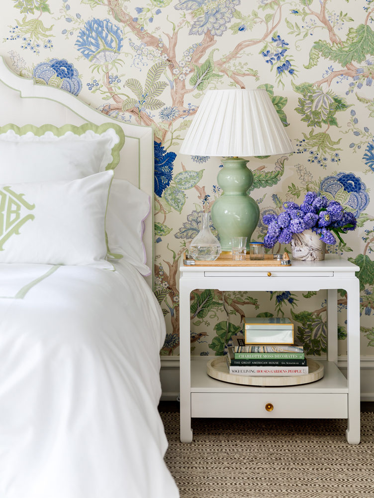 White side table with green table lamp, marbled vase, in bedroom with floral wallpaper
