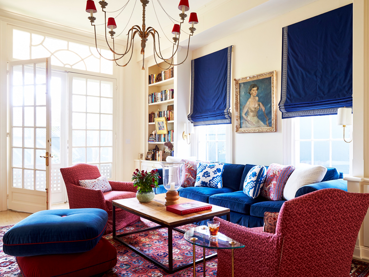 Eclectic living room matches a blue sofa with drapes and red patterned armchairs