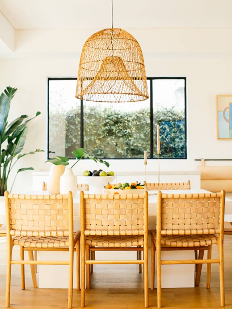 Woven dining chairs and white dining table under a wicker ceiling lamp