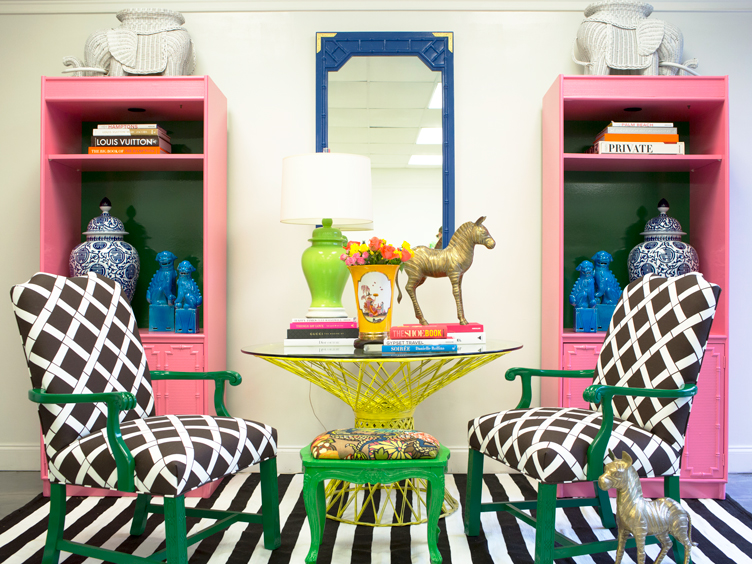 Maximalist sitting area mixes patterned accent chairs, striped rug, yellow side table, and pink bookshelves.