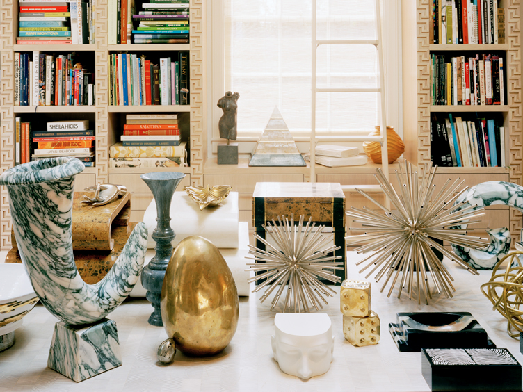 Marble table with gold, brass, and marble trinkets including starburst sculpture, oversized dice, and a gold egg.