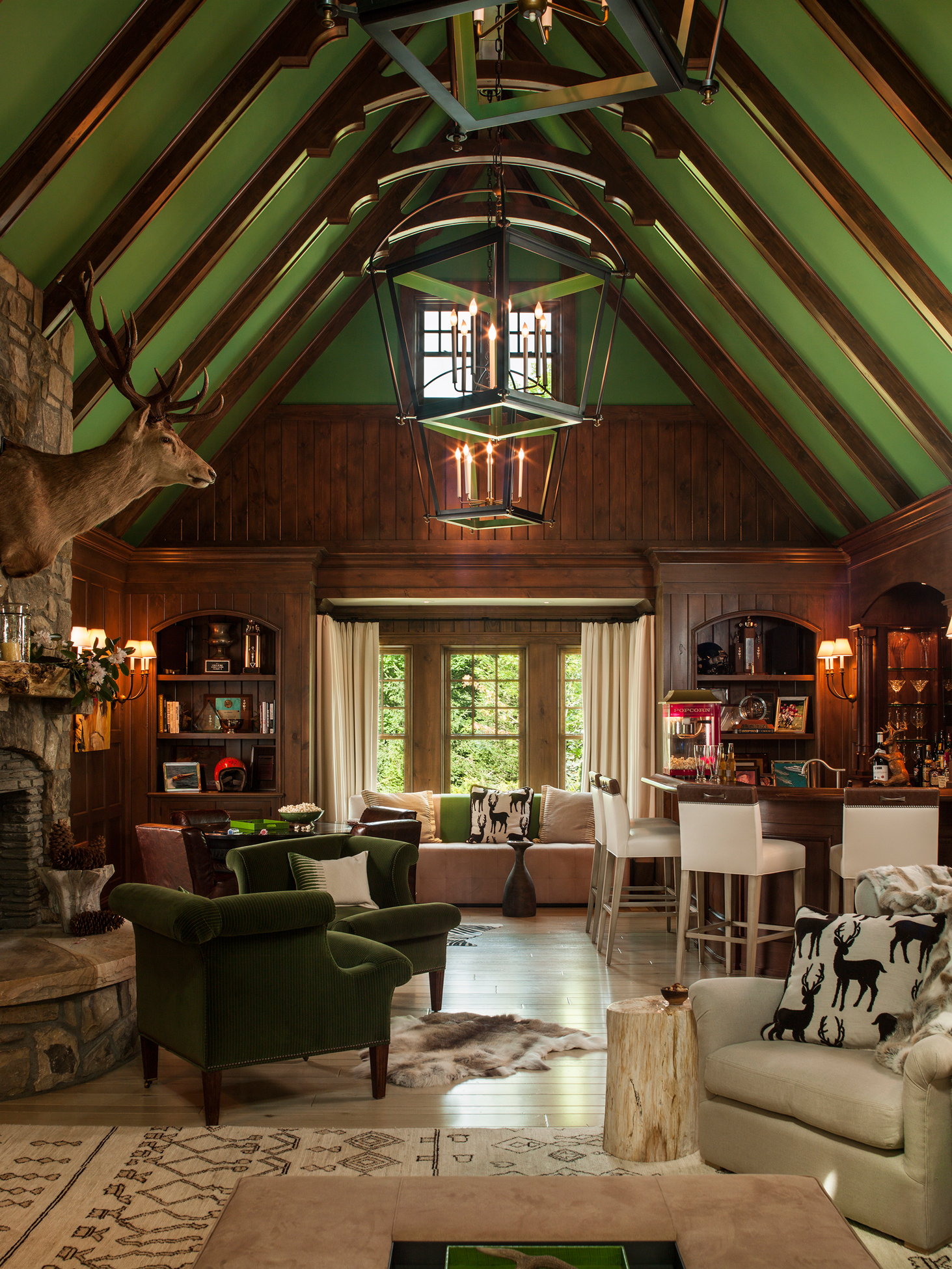 Wood cabin with bold green ceiling, green velvet accent chairs, and wood paneling.