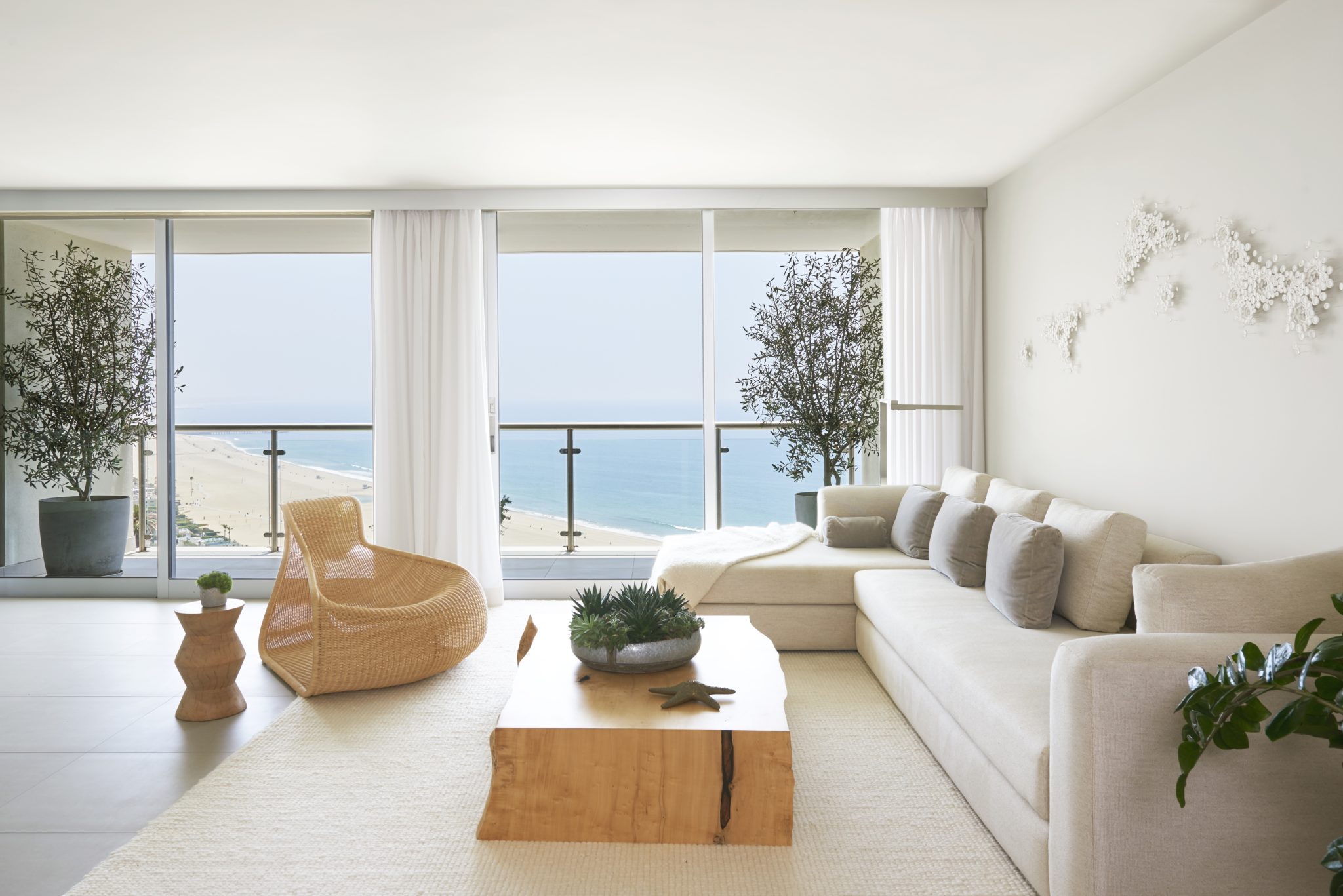 A Santa Monica penthouse with white sectional, wicker accent chair, and solid wood coffee table