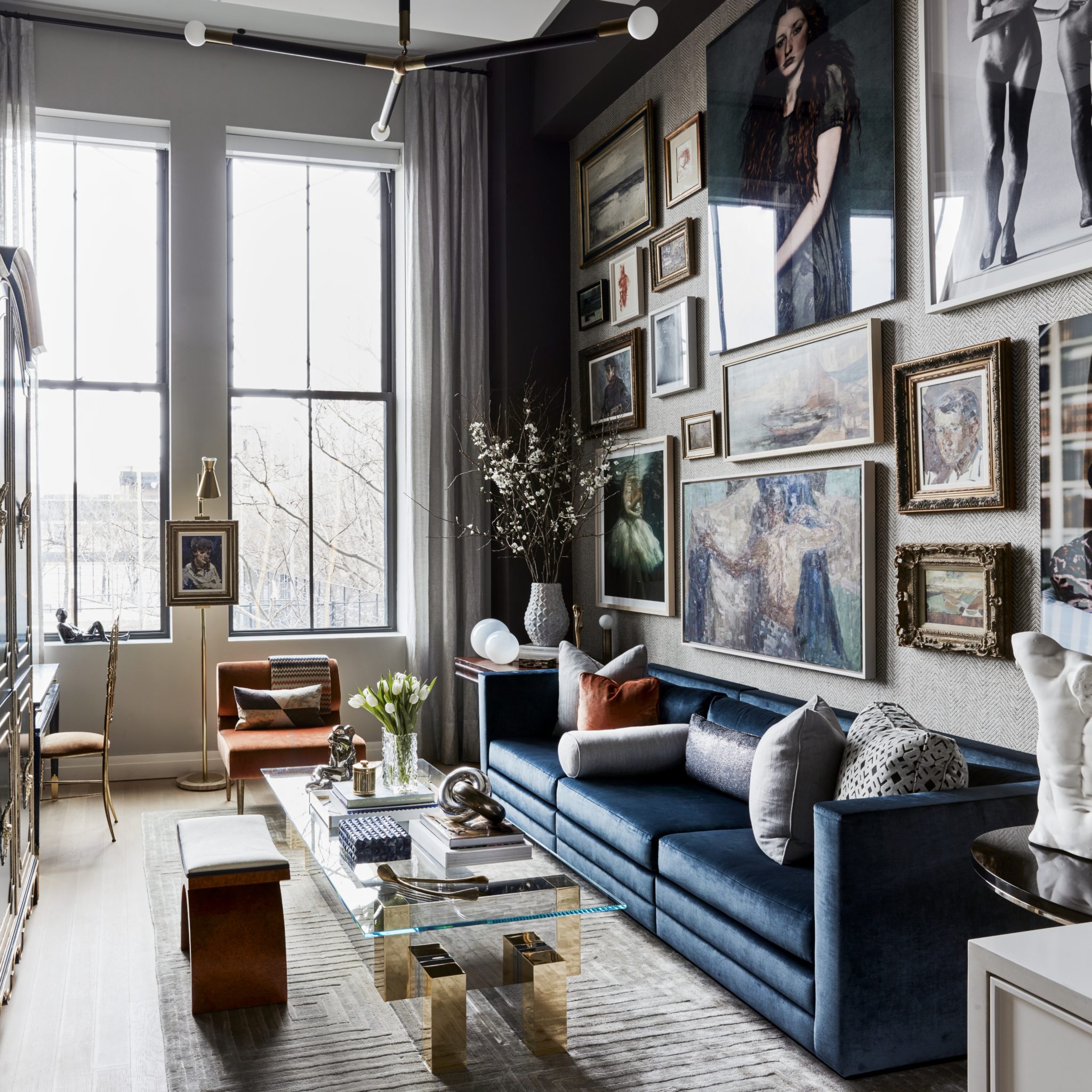 Cozy sitting room with blue velvet sofa under a gallery wall of vintage paintings 