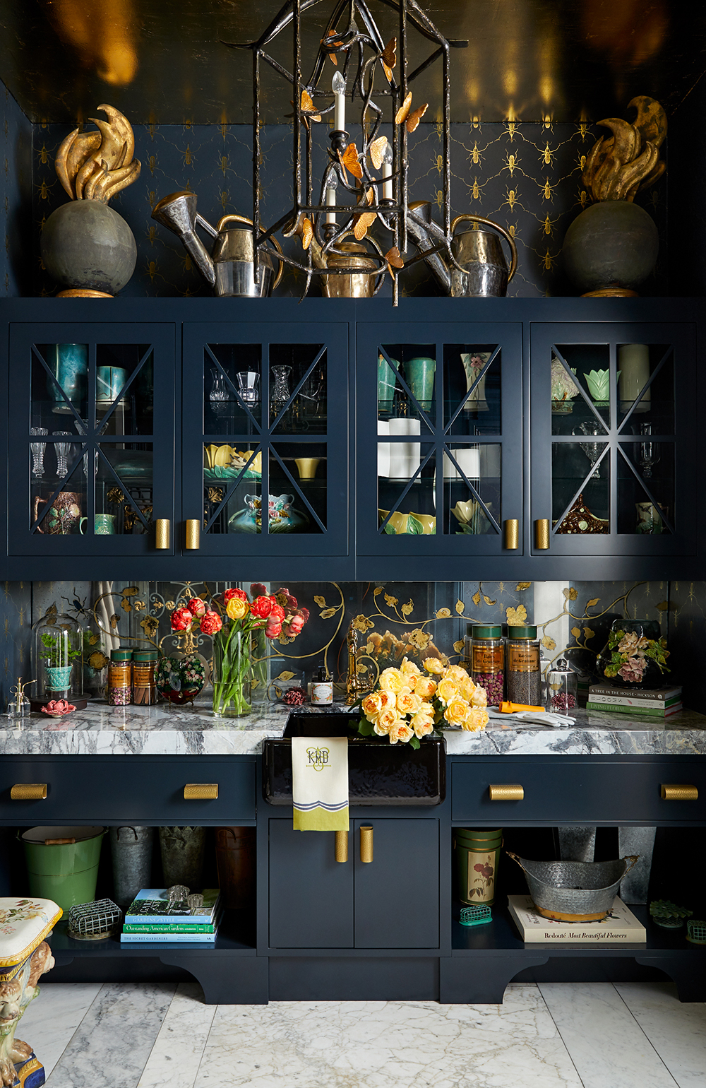 Dark blue butlers pantry with glass-doored cabinets and floral arrangements. 