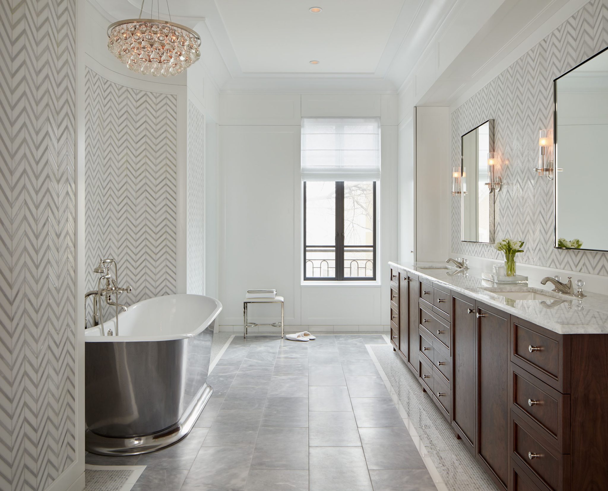 Bight bathroom with silver soaking tub and glass chandelier with brown wood vanity 