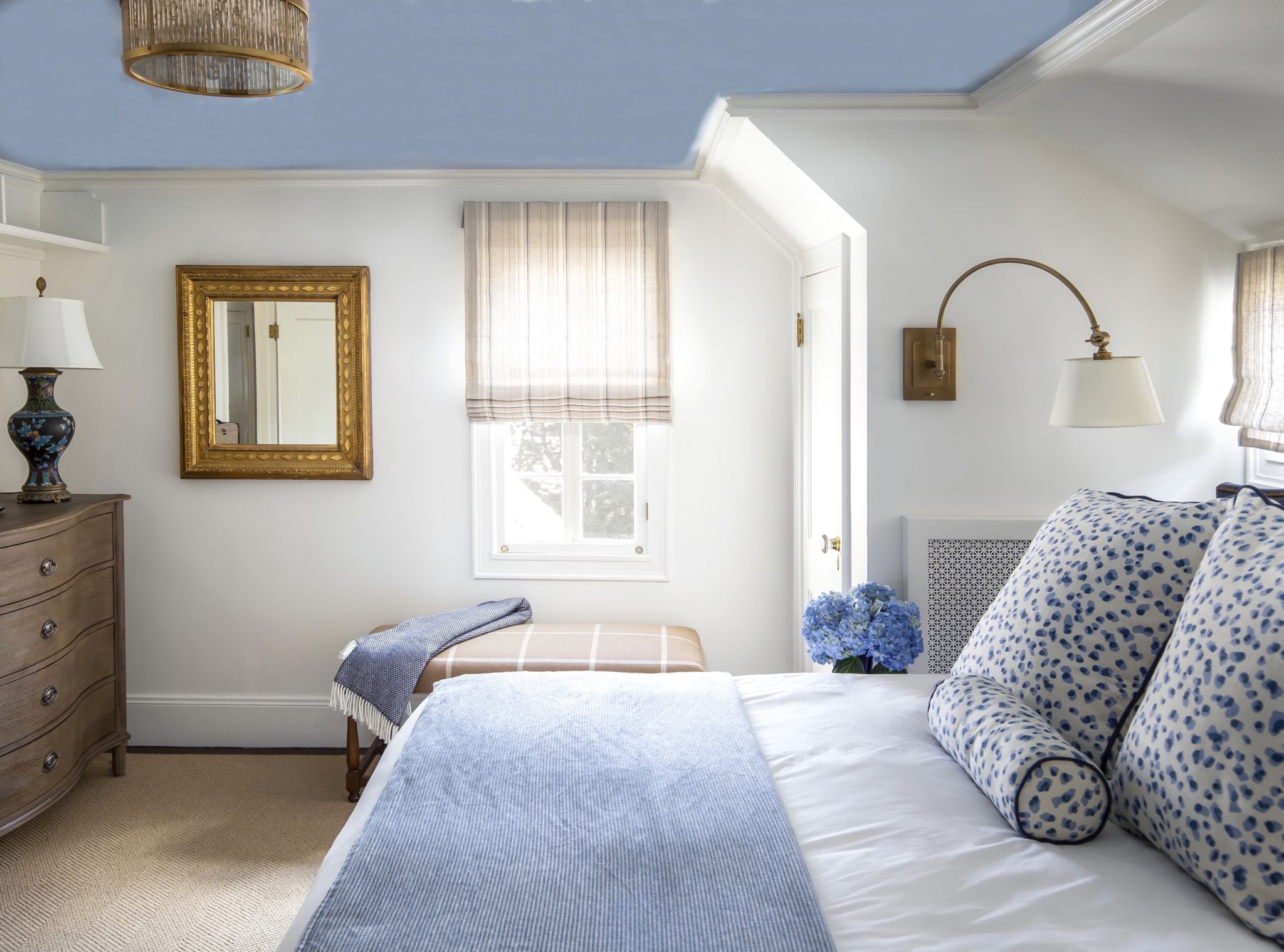 Beachy bedroom with blue-patterned throw pillows and gold-framed mirror