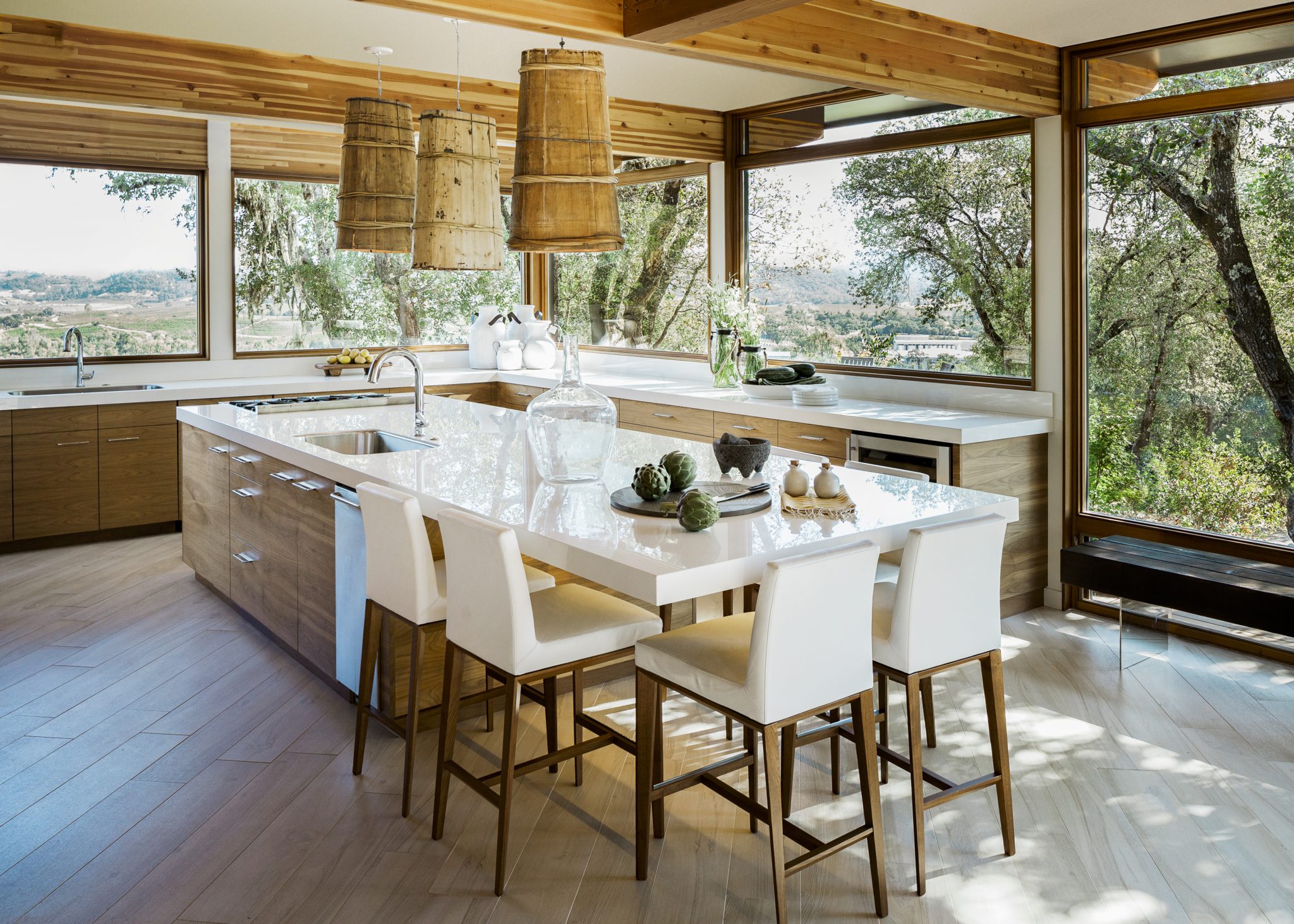 This bright kitchen mixes natural wood cabinets with glossy white countertops and repurposed barrel light fixtures.