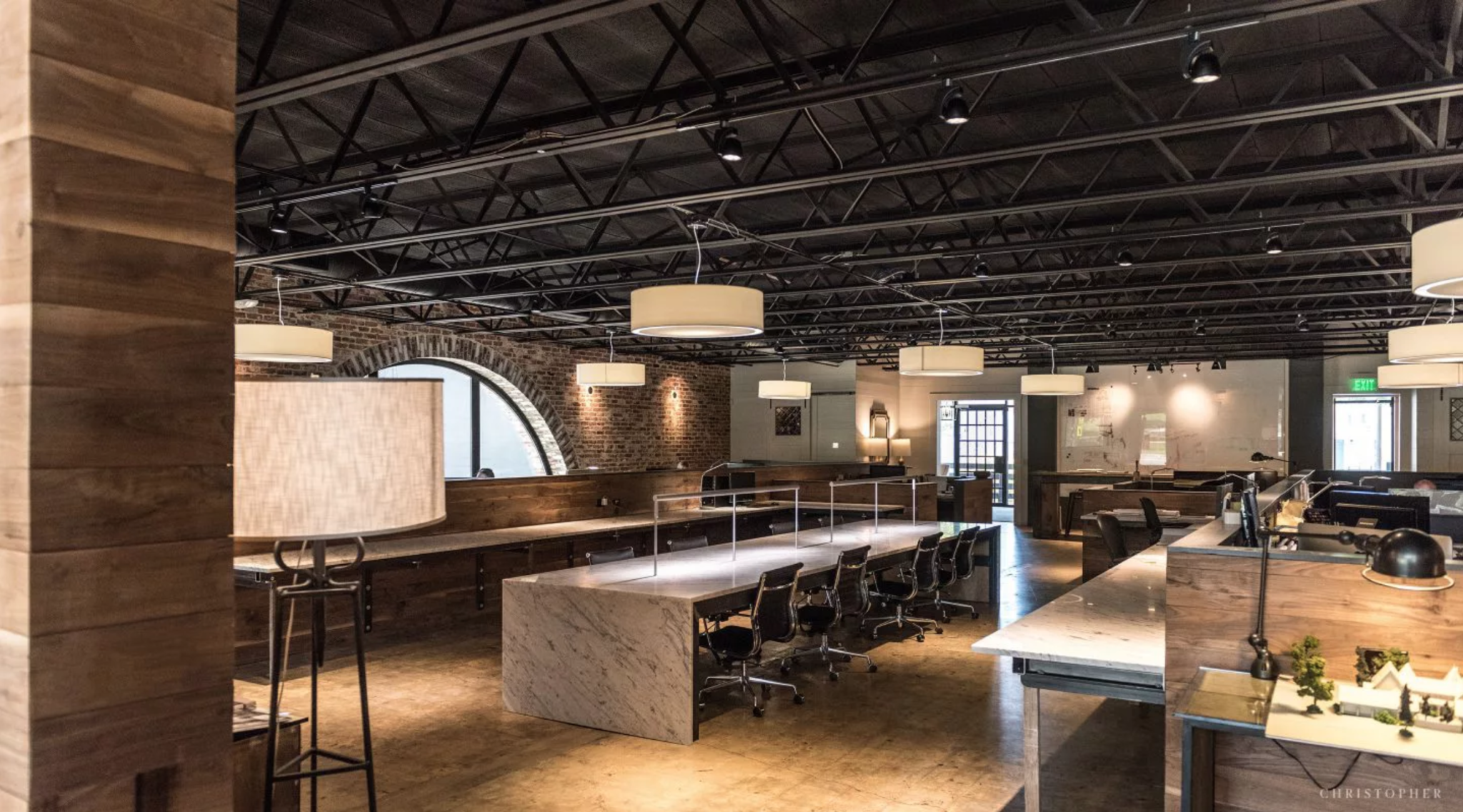 Industrial office space with marble desks, wood features, and industrial ceiling lights.