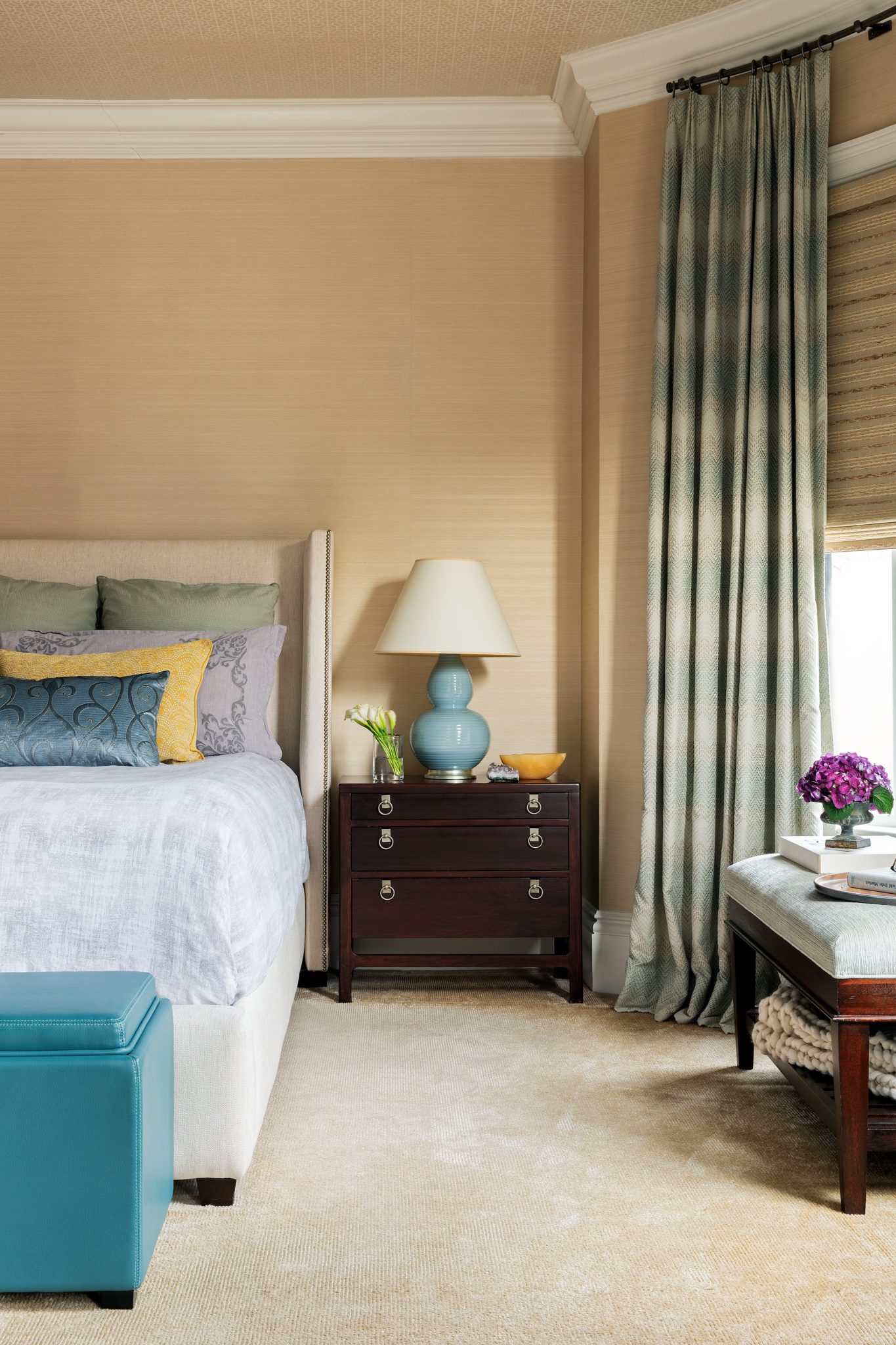 Bedroom with dark wood side table and light, neutral tones in the bedding, drapes, and rugs.