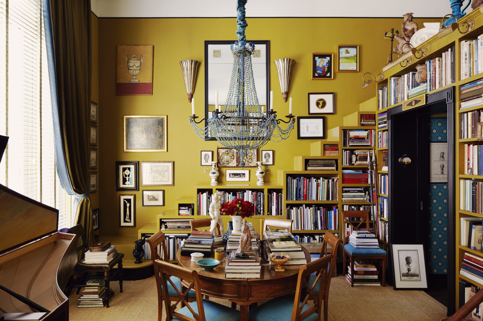 Yellow dining room surrounded by books and a beaded chandelier 