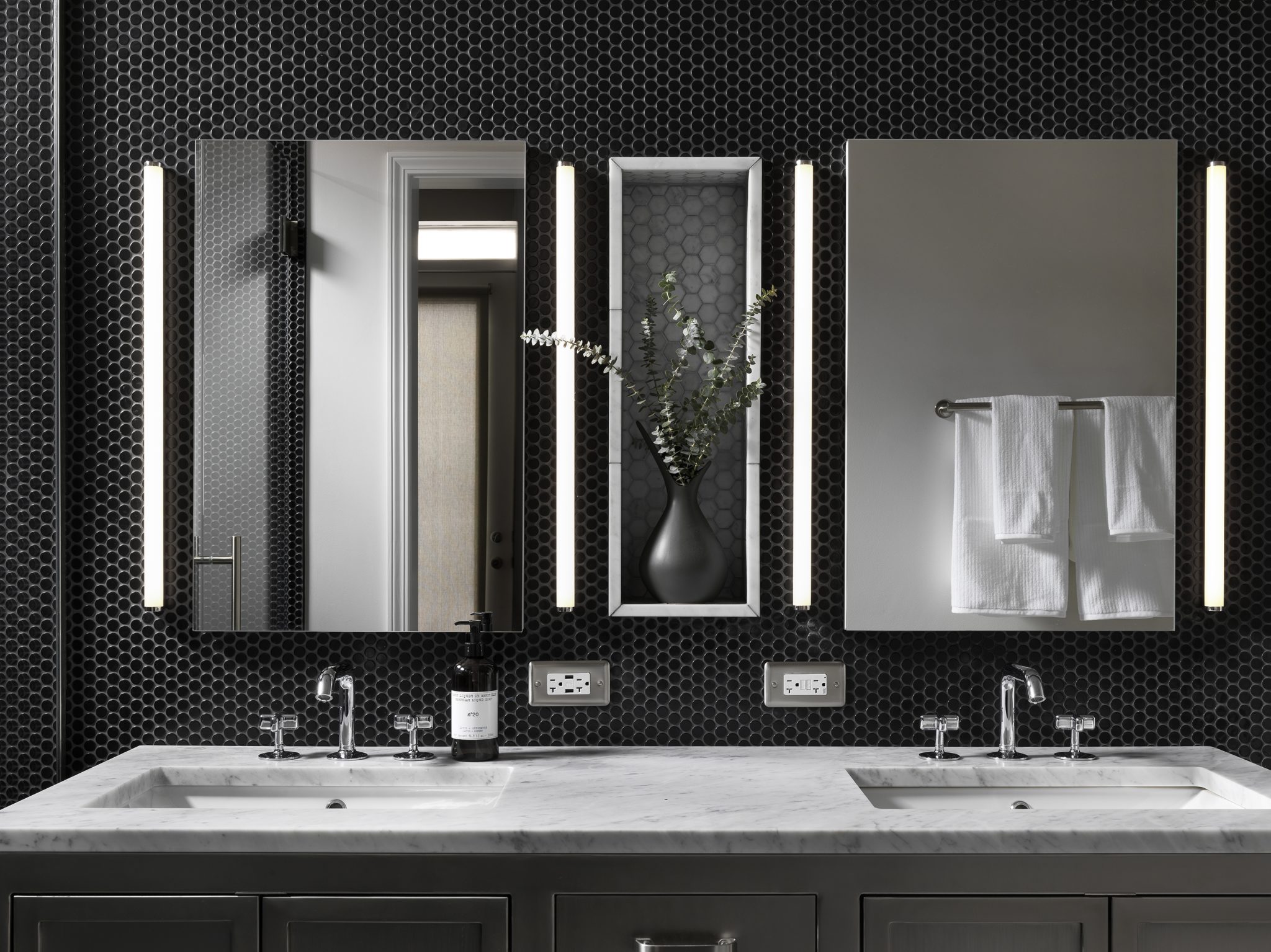 Sleek bathroom with black wall tiles and black vase of eucalyptus 