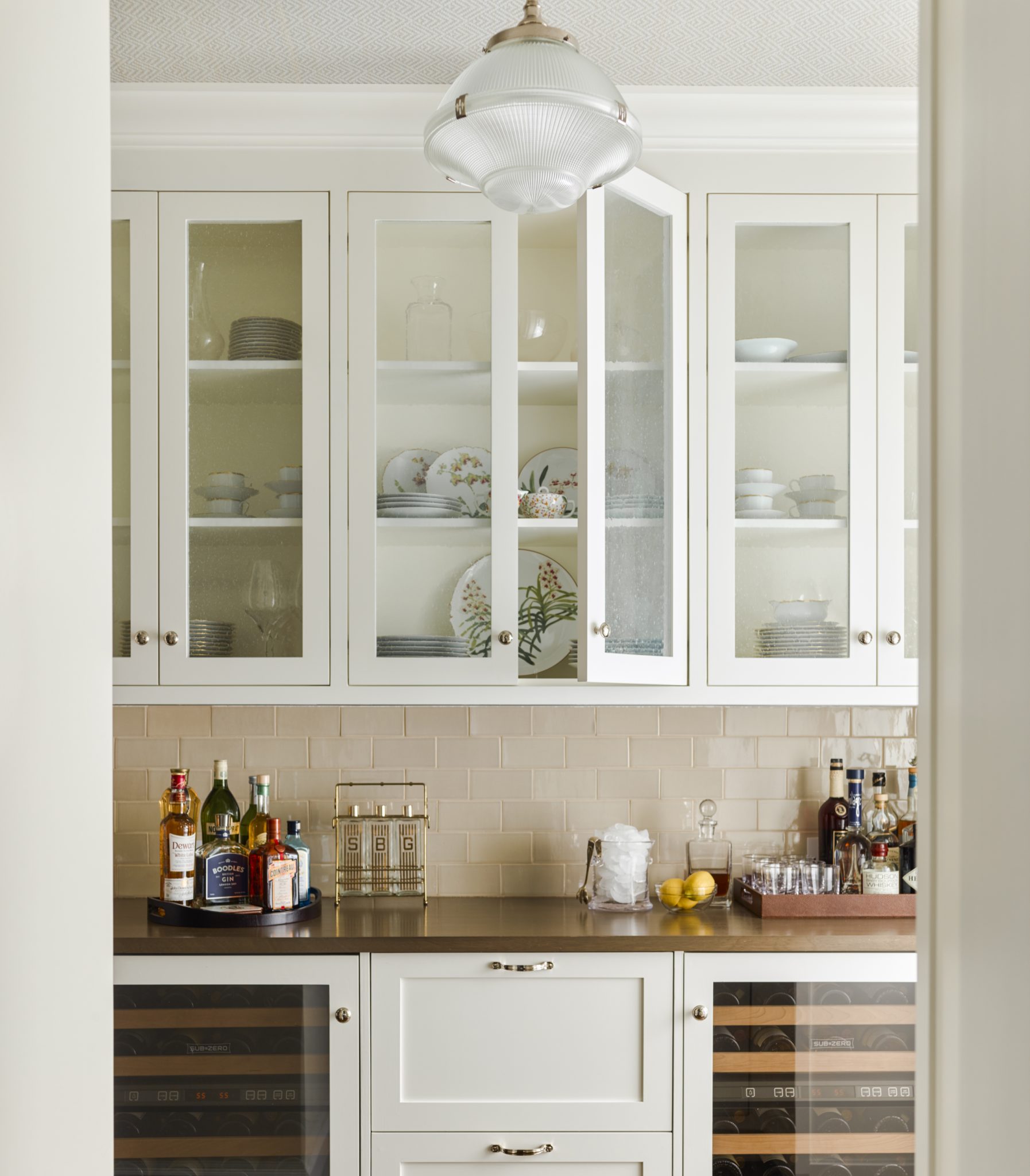 Bright home bar with glass-faced white cabinets with china and bar trays