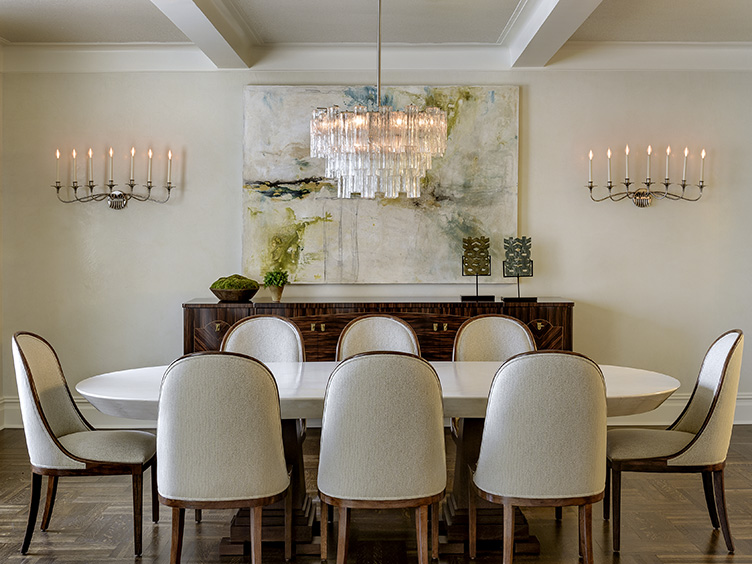 Elegant dining room with wall-mounted candelabras, crystal chandelier, and white upholstered dining chairs