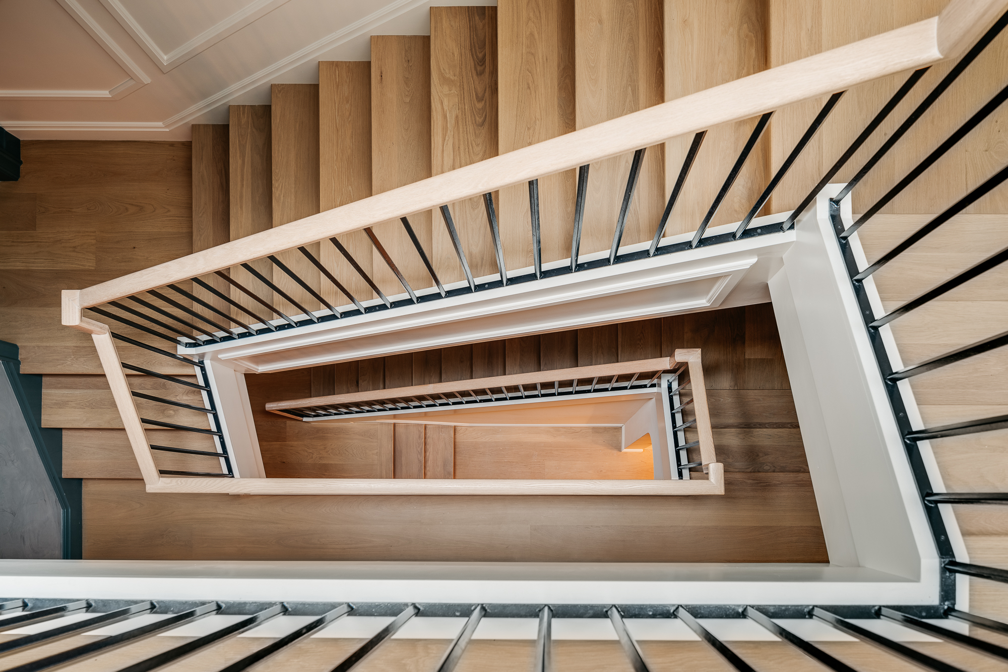 Natural wood staircase with black and wood railings and white paneled walls.